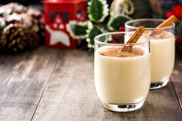 Homemade eggnog with cinnamon in glass on wooden table. Typical Christmas dessert.
