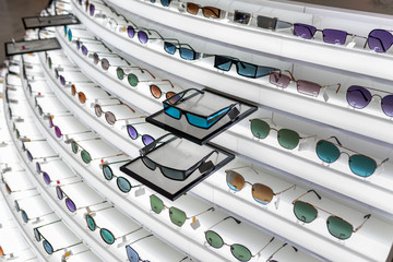 A large selection of optics located on a retractable white stand with various sunglasses of different shapes. Choice. The concept of optics. Eyes. Glasses.