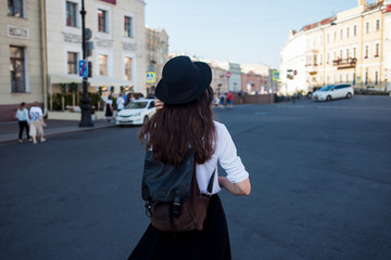 Young woman in hat walking in city, back view. Girl tourist enjoys the walk.