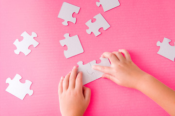 children's hands fold a paper white puzzle on a pink background development of fine motor skills of hands