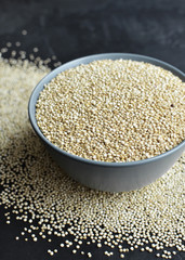Dry organic quinoa seeds in ceramic bowl on dark concrete background