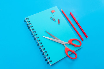 Blue notebook with black rings with a red felt-tip pen and pencil and red scissors lying on the...