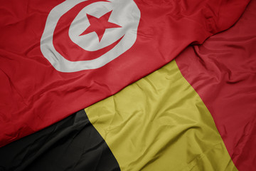 waving colorful flag of belgium and national flag of tunisia.