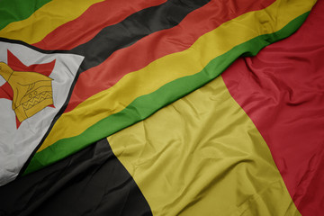 waving colorful flag of belgium and national flag of zimbabwe.