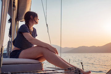 attractive young woman in a striped t-shirt enjoys the sunset on the deck of a sailing yacht. Girl...