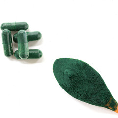 spirulina algae powder in a wooden spoon and spirulina capsules on a white background.