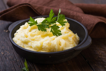 Mashed potatoes or boiled puree with parsley  in cast iron pot on dark wooden rustic background.  top view