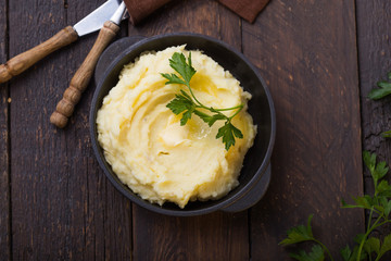 Mashed potatoes or boiled puree with parsley  in cast iron pot on dark wooden rustic background. ...