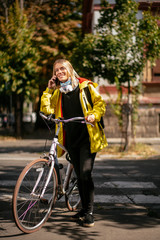Young woman using phone while walking on the street. Portrait of girl with bicycle. 