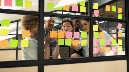 Diverse workers creating and assigning projects using multicolored sticky notes