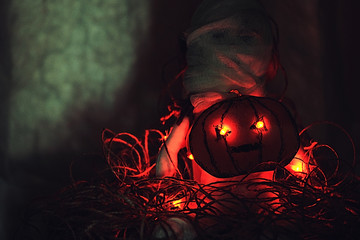 A mummy doll sits in the ropes behind a painted pumpkin with burning eyes. Film grain. Grunge...
