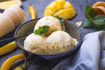 Close up bowl with vanilla ice cream covered with caramel sauce chilli pepper and fresh mango fruit on dark background. Selective focus. Summer dessert