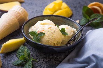 Close up bowl with vanilla ice cream covered with caramel sauce and fresh mango fruit on dark background. Selective focus. Summer dessert
