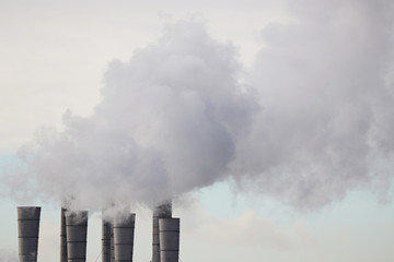 Air pollution, smoking pipes on blue sky background. Factory chimneys, concept of industry and ecology, steam plant, heating season, global warming