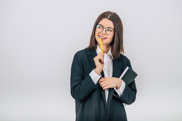 Pretty young businesswoman in black suit standing, notebook and pen in her hands, thinking what to write.