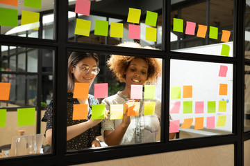 Multi racial businesswomen writing on sticky notes new startup ideas