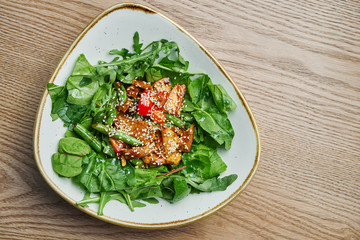 Close up view on tasty Light warm salad with tomato, turkey, a mix of greens in stylish grey bowl. Tasty lunch. Wooden background
