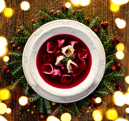 Christmas beetroot soup, red borscht with small dumplings with mushroom filling in a ceramic white plate on a wooden table, top view. Traditional Christmas eve dish in Poland. 