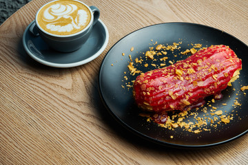 Appetizing and large eclair with glaze of raspberry on top and fir cream inside on a black plate....