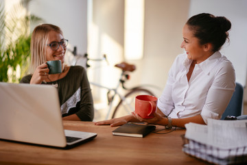 Two young women having coffee break in office