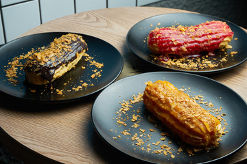 Three Appetizing and large eclair with glaze of on top and fir cream inside on a black plate....