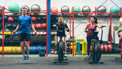 Group of athletes doing air bike and skipping rope at the gym