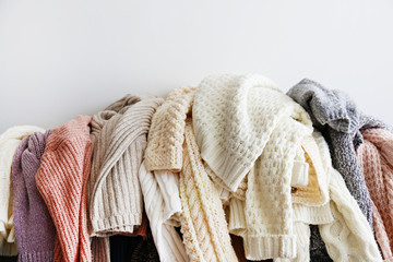 Categorizing winter laundry concept. A messy pile of kniwear lying on grey textile sofa. Bunch of unfolded sweaters prepeared for sorting. Close up copy space, background.