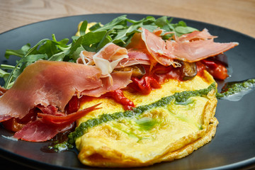 Frittata with prosciutto, pesto sauce, arugula and bell pepper on black plate. Tasty and healthy lunch. Omelette