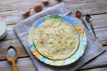 Omelet in colorful plate on textile cover with ingredients on wooden background