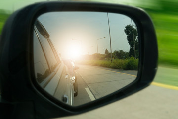Close beside car form mirror view with other cars and sun light on the road.