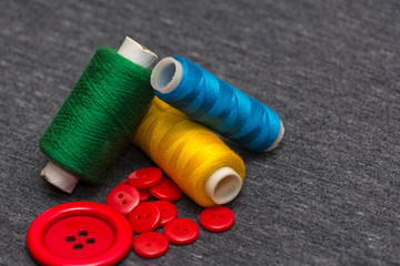 Colorful bright threads for sewing and red buttons. Gray blurred background. Sewing industry. Atelier design elements.
