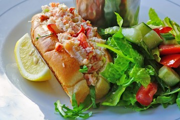 A lobster roll sandwich with a green salad and French fries