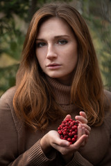 Red-haired girl with skin covered with bright freckles, with a sprig of red mountain ash in her hands 