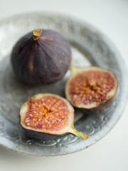 Two ripe figs. One whole fig and the second cut in half on a white table.