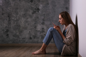 Portrait of beautiful young woman with depressed facial expression sitting in the corner holding...