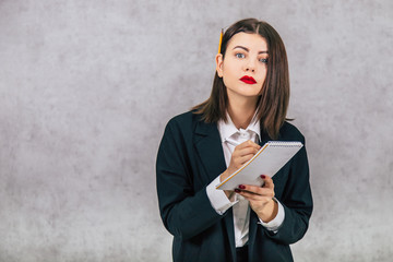 Cute concentrated business women standing with pencil behind her ear and listening, writing down something into the notebook