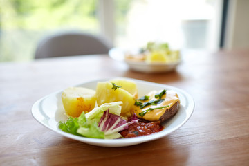 Boiled potatoes with green salad, vegetables and cutlet. Plate with homemade food on a wooden dinner table. Cooked potato dish