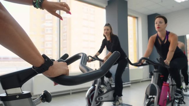 Women group spinning bike at bicycle gym in fitness club. Fitness woman on bike training. Female hands of sport woman showing thumb down on cycling class in studio.