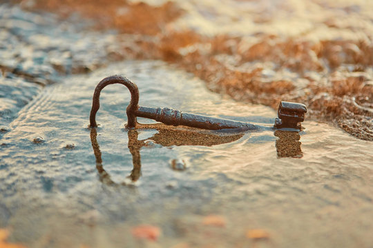 An old rusty lost treasure key, lying in the sand in the surf on the beach.  The concept of luck and unexpected wealth.