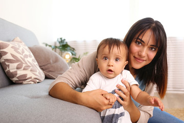 Portrait of young mother taking care of her little son at home. Beautiful female with straight brunette hair playing with child at living room. Close up, copy space, background.