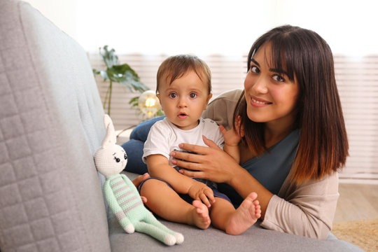Portrait of young mother taking care of her little son at home. Beautiful female with straight brunette hair playing with child at living room. Close up, copy space, background.
