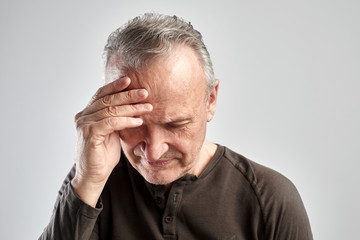 elderly gray-haired man with expression of pain on face put his hand on head, feels dizzy and...