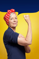 Senior rosie riveter concept: mature woman with clenched fist rolling up her sleeve, background...
