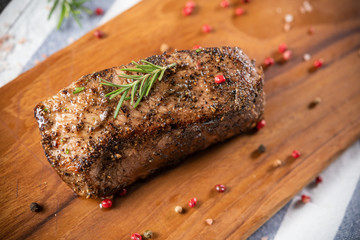 Full piece of beef steak with black pepper, not yet cut on a wooden chopping board with rosemary leaves and many spices, beautiful decorated, gray-white napkin background. Good food for good health