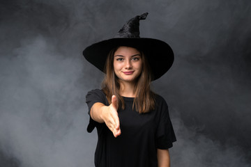 Girl with witch costume for halloween parties over isolated dark background handshaking after good deal