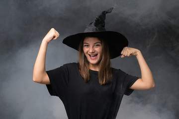 Girl with witch costume for halloween parties over isolated dark background celebrating a victory