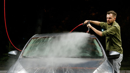 Young man washing his car in car wash. Cleaning Car Using High Pressure Water. Washing with soap.