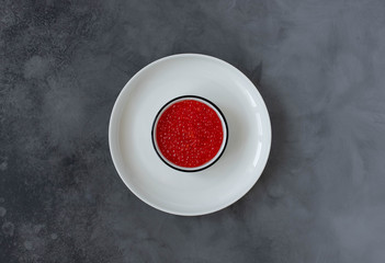 red caviar in a white plate on a dark background. top view. copy space