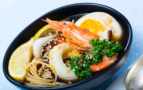 Photography of plate with spicy pan-Asian soup with squid, shrimp, egg noodles and sesame
