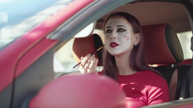 Mime paints her lips with red lipstick winking at the camera.